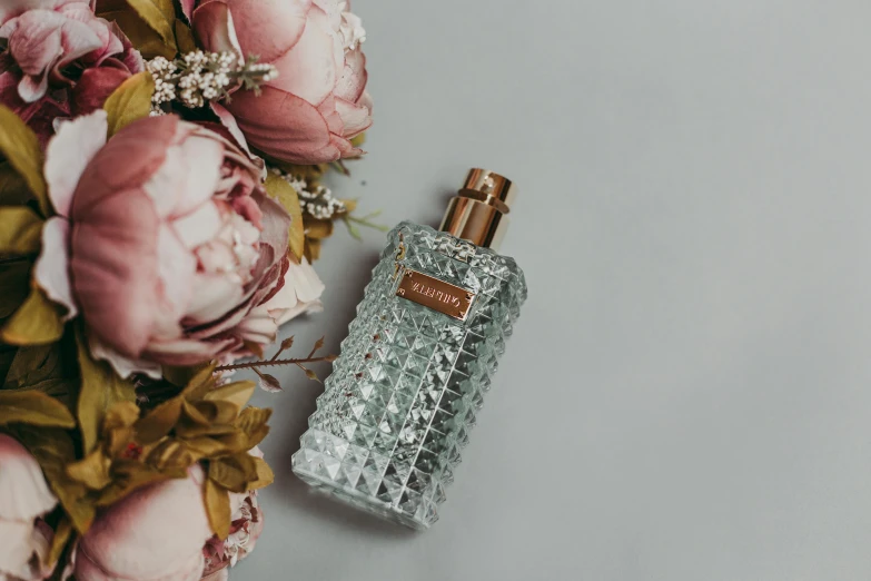 a bottle of perfume next to a bouquet of flowers, by Matija Jama, pexels contest winner, delicate patterned, on a gray background, bottle of vodka, tufted softly