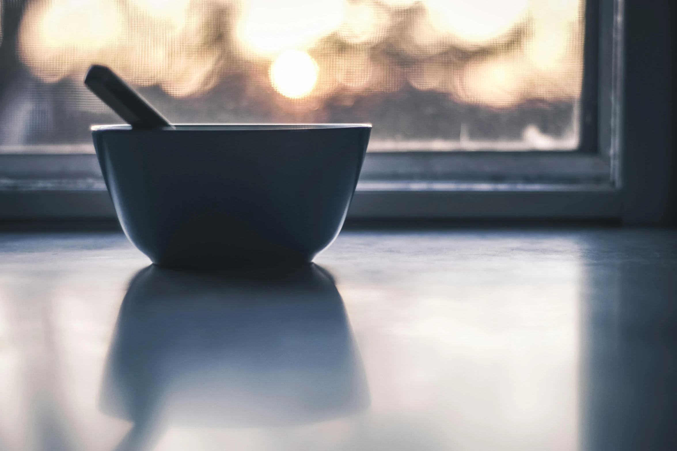 a bowl sitting on top of a table next to a window, unsplash, pestle, plain background, in the evening, spoon