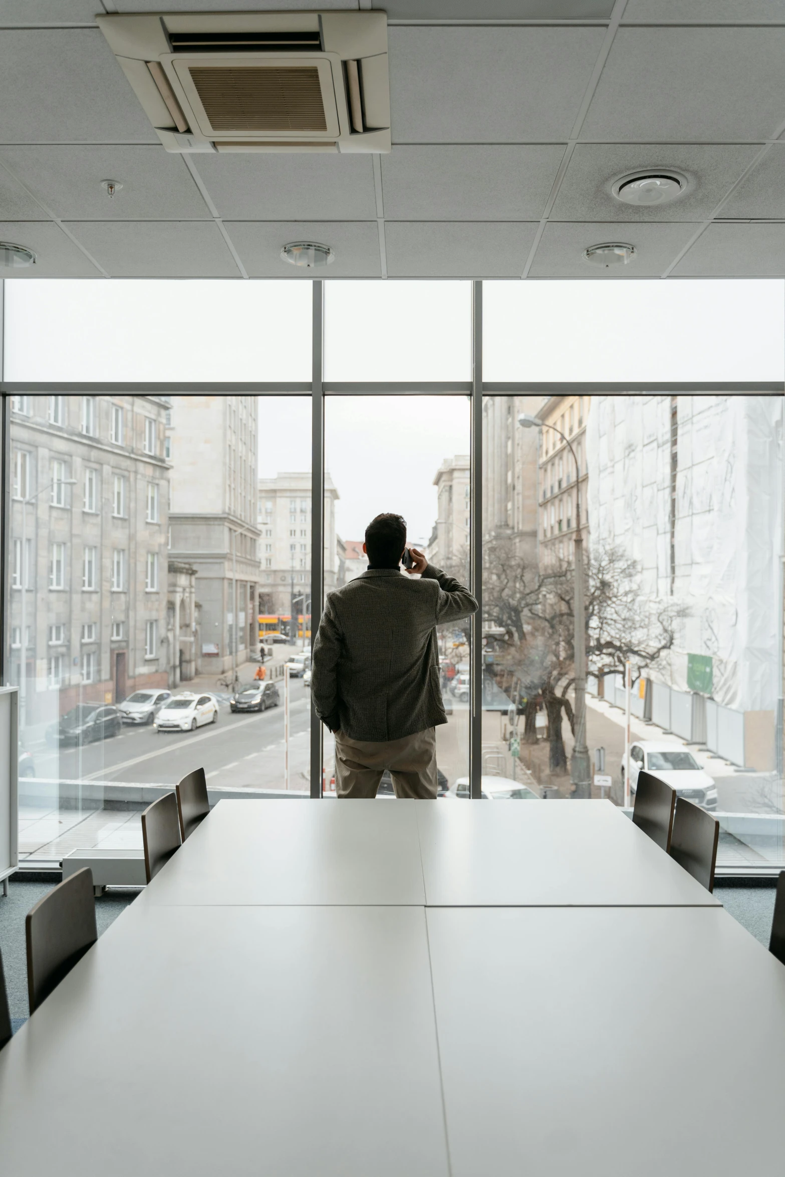 a man standing in front of a large window, a picture, unsplash contest winner, office background, long shot from back, on a white table, looking off into the distance