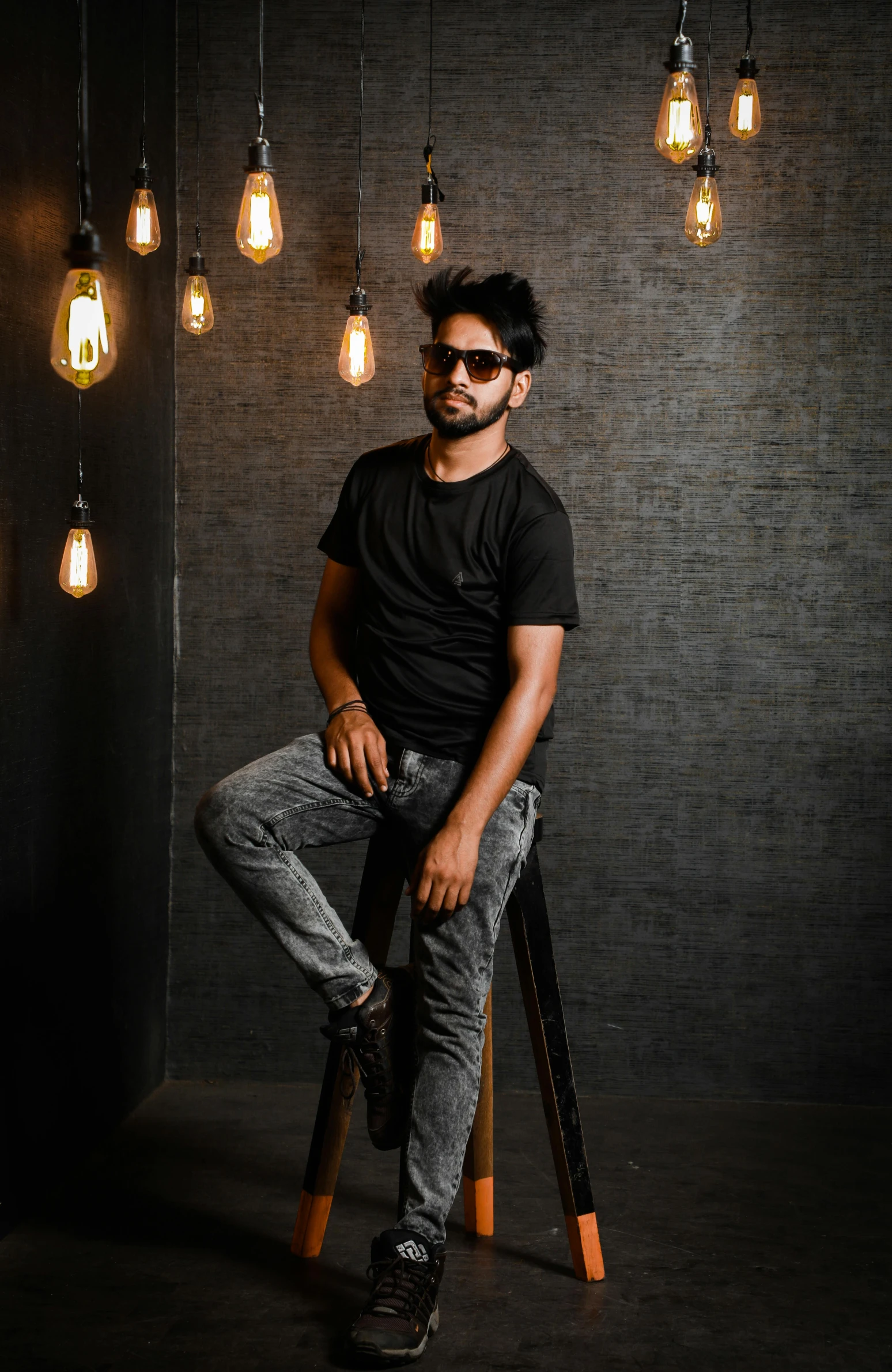 a man sitting on a stool in front of a bunch of light bulbs, a portrait, by Manjit Bawa, pexels contest winner, wearing a dark shirt and jeans, isolated background, portait photo profile picture, trending on artstion