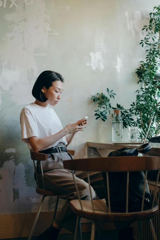 a woman sitting at a table using a cell phone, by Jang Seung-eop, trending on unsplash, dressed in a white t-shirt, sittin, tall, asian human