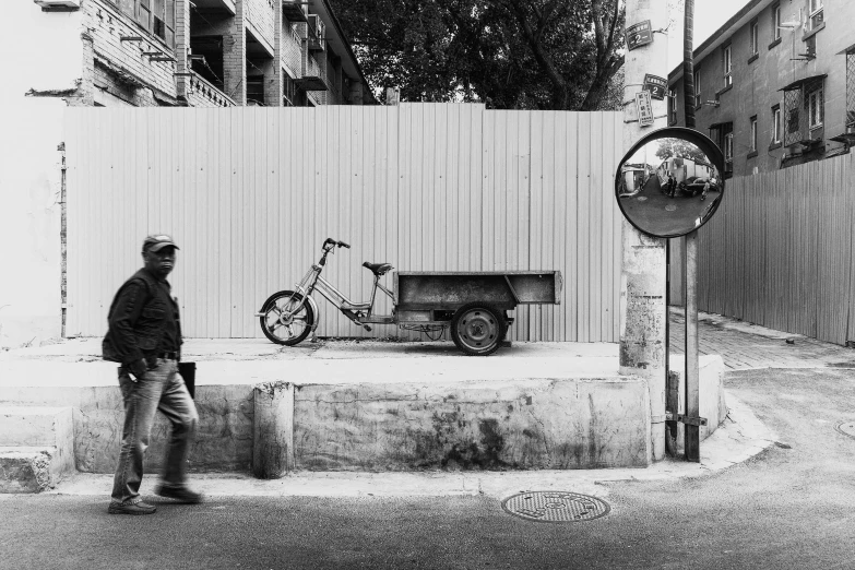 a black and white photo of a man walking down the street, by Paolo Parente, garbage wheel bin, on a wall, tehran, moped