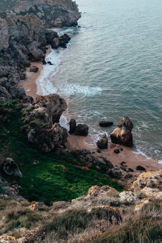 a man standing on top of a cliff next to the ocean, pexels contest winner, baroque, top down view, portugal, subtle colors, grass and rocks