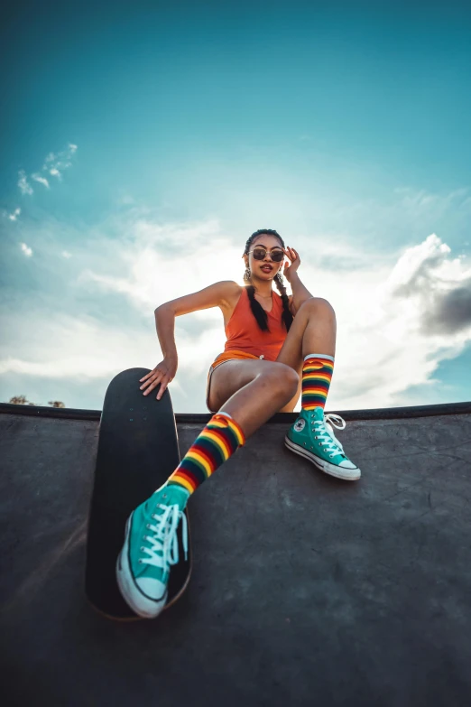 a woman sitting on top of a skateboard on a ramp, trending on pexels, striped orange and teal, wearing kneesocks, sunglasses, bright sky