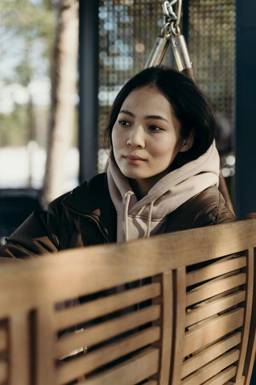 a woman sitting on top of a wooden bench, a portrait, unsplash, hyperrealism, star trek asian woman, model wears a puffer jacket, still from the film, sitting in a cafe alone