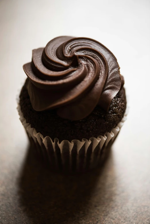 a chocolate cupcake sitting on top of a wooden table, up-close, david kassan, snacks, swirls