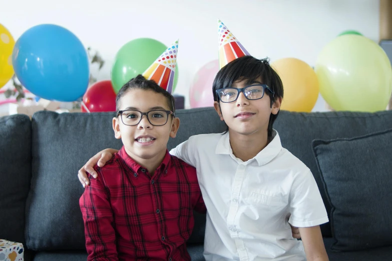 a couple of kids sitting on top of a couch, square rimmed glasses, at a birthday party, portrait image, neuroscience