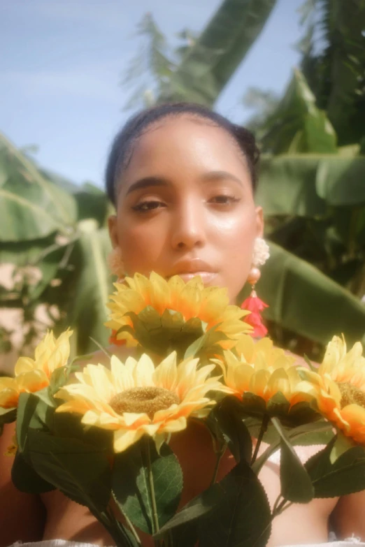 a woman holding a vase filled with yellow flowers, an album cover, unsplash, realism, jamaica, sunflare, still from a music video, tan skin