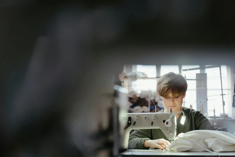 a young boy working on a sewing machine, unsplash, stood in a factory, digitally enhanced, ignant, natural lighting