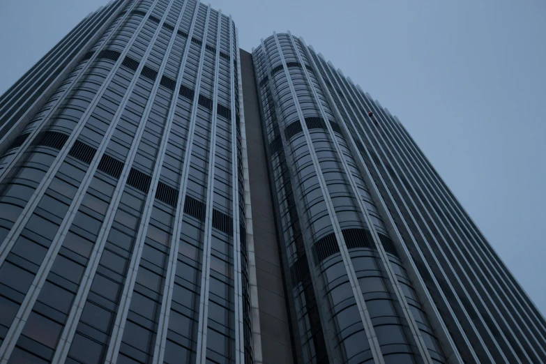 a couple of tall buildings next to each other, inspired by Zaha Hadid, pexels contest winner, bauhaus, grey, mysterious exterior, towering high up over your view, a pair of ribbed