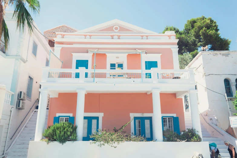 a couple of people that are standing in front of a building, by Carey Morris, pexels contest winner, neoclassicism, pink white turquoise, seashell house, greek setting, blue and orange palette