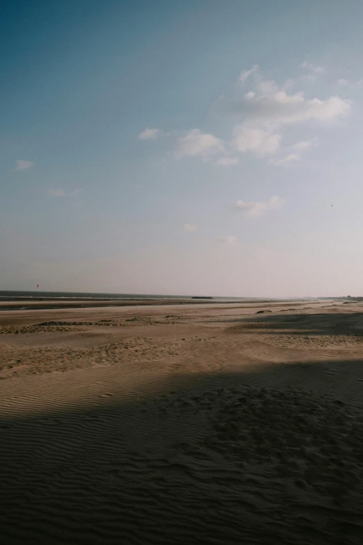 a man flying a kite on top of a sandy beach, by Jacob Toorenvliet, land art, distant - mid - shot, helmond, afar, low quality photo