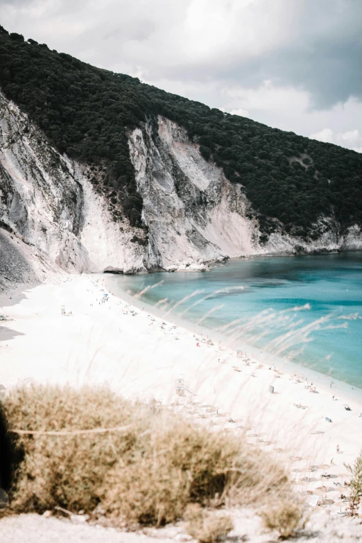 a man standing on top of a sandy beach next to a body of water, unsplash contest winner, renaissance, steep cliffs, greek nose, square, bleached colors