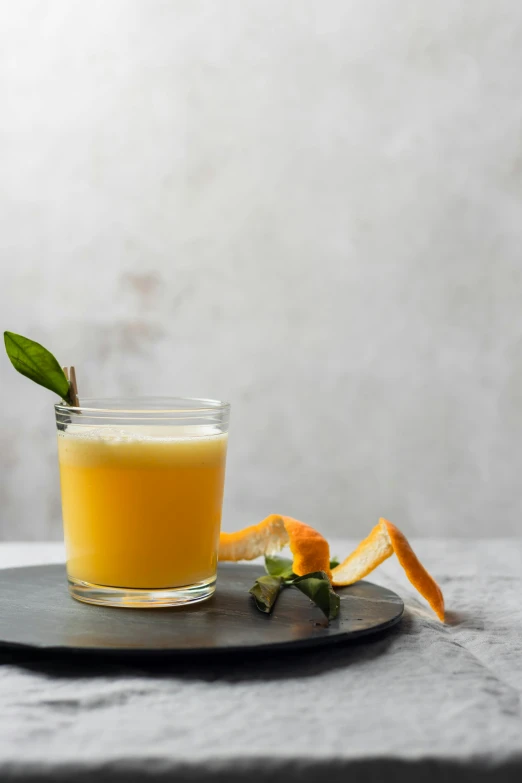 a glass of orange juice on a plate, a portrait, inspired by Jacopo Bellini, shutterstock, on a gray background, ivy's, rum, vanilla