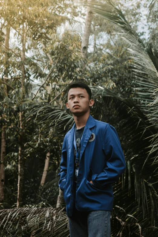 a man standing in the middle of a forest, an album cover, unsplash, sumatraism, wearing blue, portrait of young man, mechanic, lush surroundings