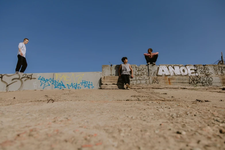 a group of people standing on top of a cement wall, an album cover, by Niko Henrichon, pexels contest winner, graffiti, sand, sitting, medium shot of two characters, 15081959 21121991 01012000 4k