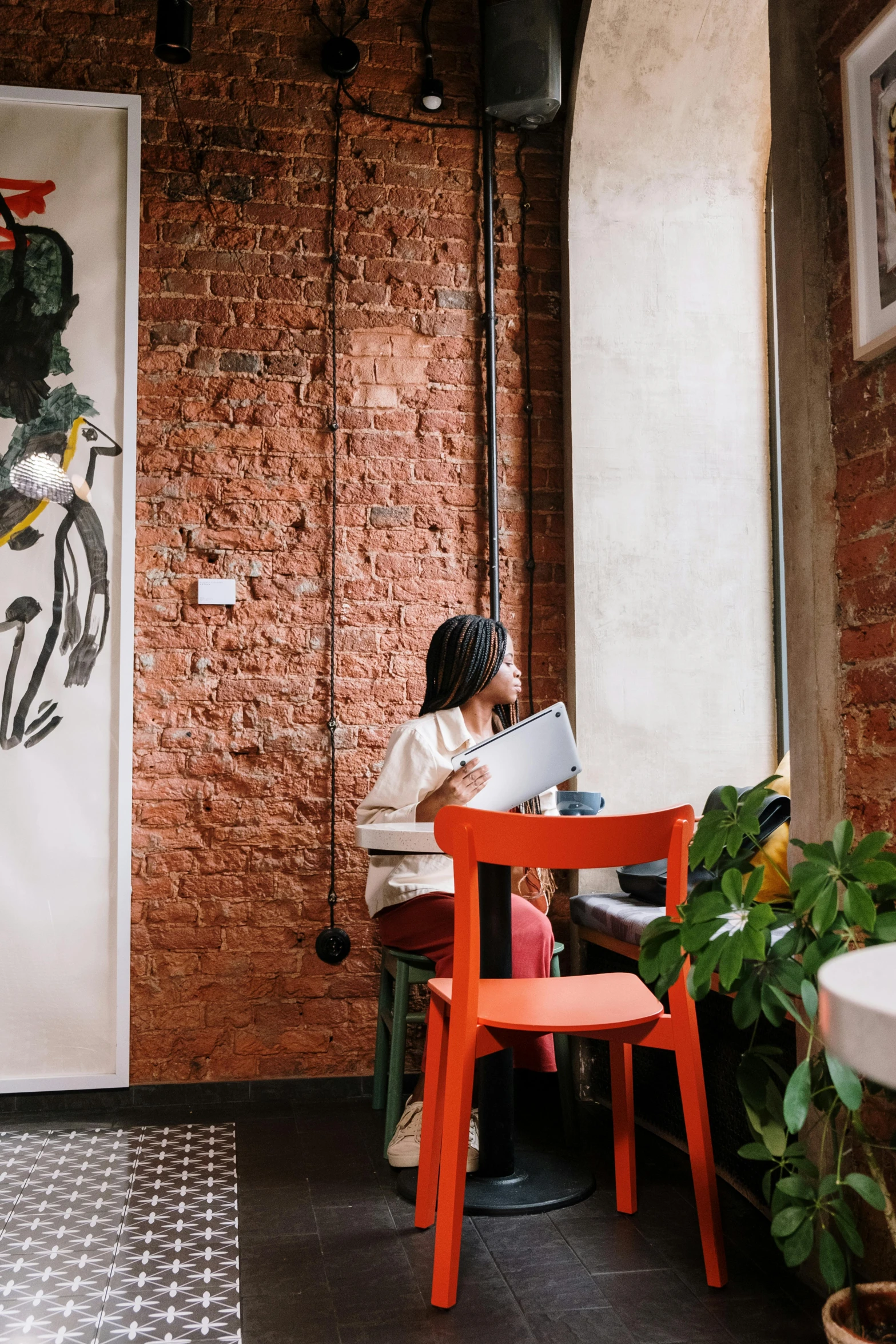 a woman sitting at a table with a laptop, by Adam Marczyński, trending on unsplash, process art, painted on a brick wall, cafe interior, long shot from back, hanging scroll on wall