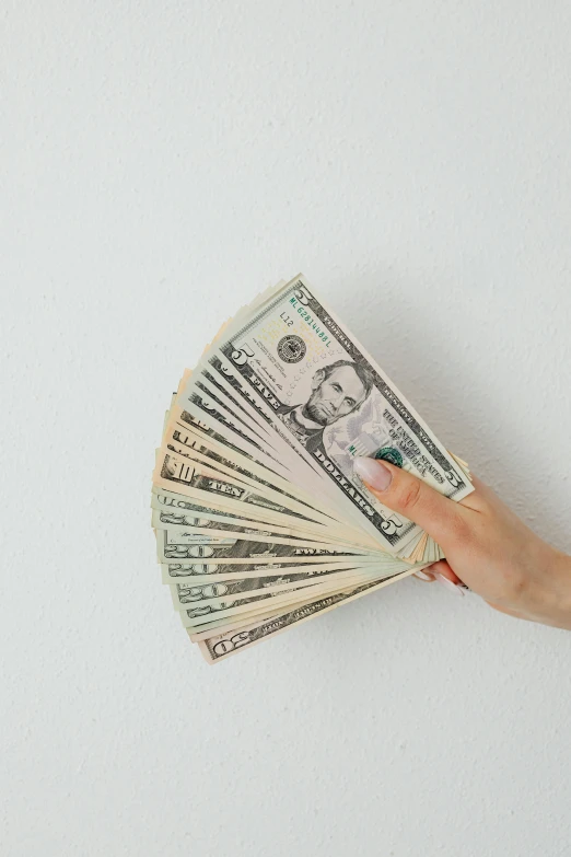 a hand holding a fan of money against a white wall, by Carey Morris, pexels contest winner, basia tran, high rendering, retail price 4 5 0, where a large