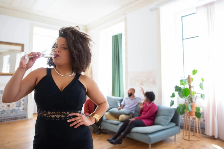 a woman in a black dress standing in a living room, pexels contest winner, happening, mixed-race woman, drinking champagne, family photo, curvy build