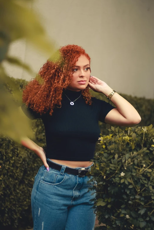 a woman with red hair standing in front of bushes, trending on pexels, doja cat, wearing a black tshirt, arm around her neck, (dark shorter curly hair)