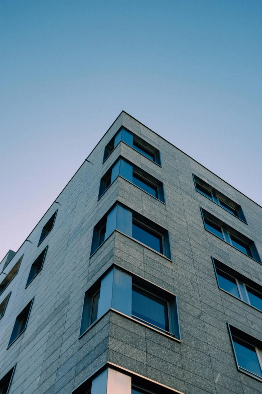 a tall gray building with lots of windows, inspired by Tadao Ando, unsplash, summer evening, clear blue sky, angled shot, square lines