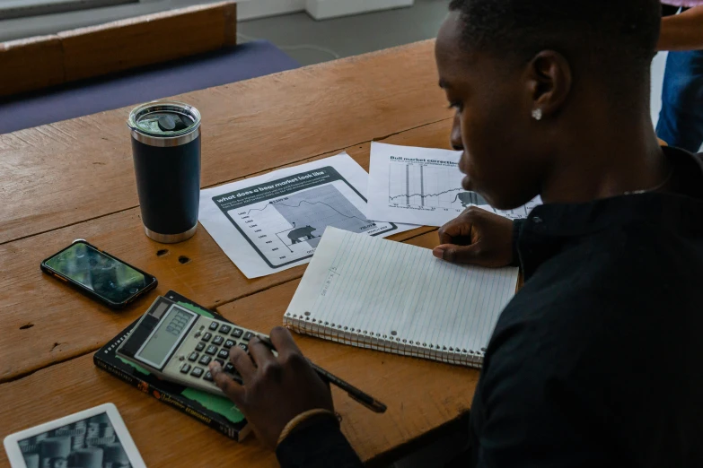 a woman sitting at a table using a calculator, by Bertram Brooker, pexels contest winner, academic art, black teenage boy, high quality screenshot, schematic in a notebook, in a workshop