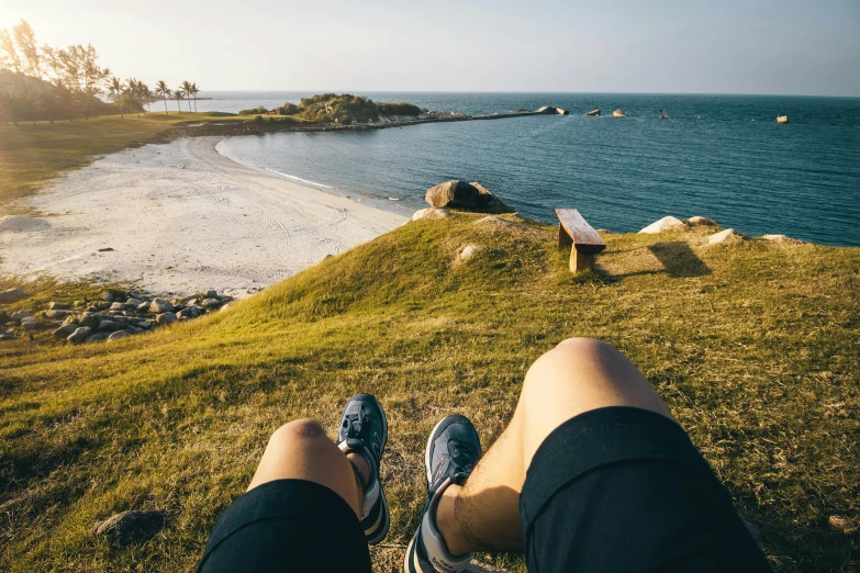a person sitting on top of a hill next to the ocean, pexels contest winner, thick legs, people resting on the grass, human back legs and sneakers, islands on horizon