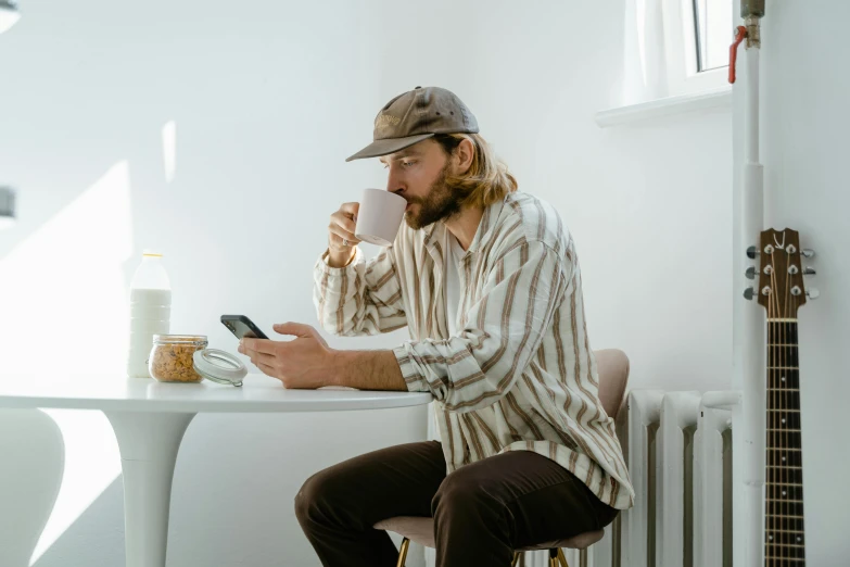 a man sitting at a table using a cell phone, trending on pexels, caracter with brown hat, wearing pajamas, felix englund, aboriginal australian hipster