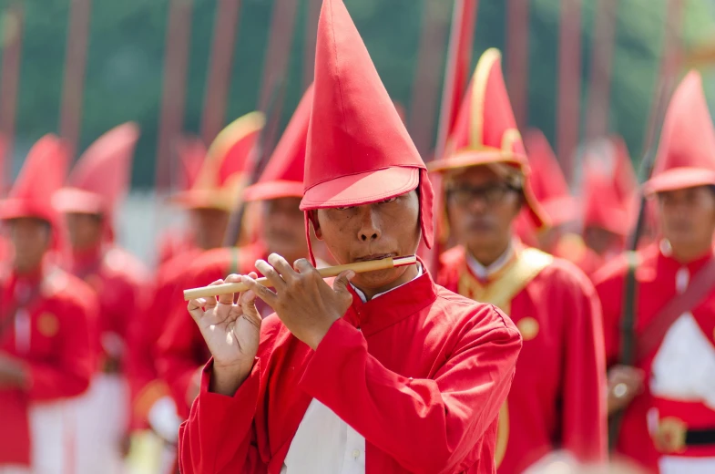 a man in a red uniform playing a flute, pexels contest winner, conceptual art, pointy conical hat, taiwan, worship of the pope, slide show