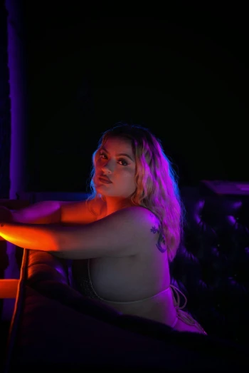 a woman sitting at a table in front of a neon sign, inspired by Nan Goldin, unsplash, renaissance, blue and purle lighting, florence pugh, in a strip club, profile image