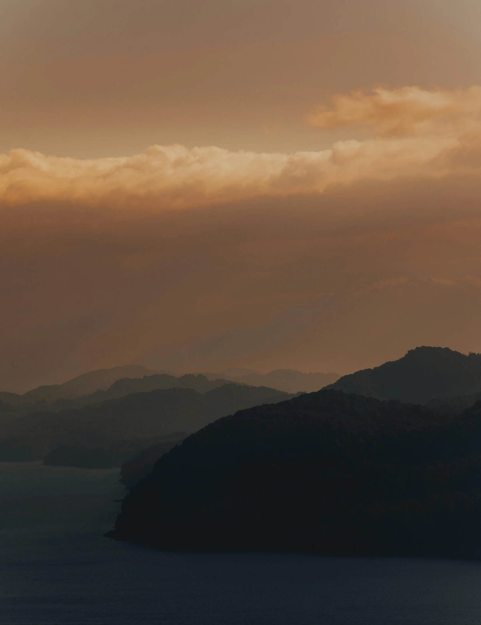 a plane flying over a large body of water, by Johannes Voss, unsplash contest winner, sumatraism, sunset in a valley, muted browns, fjords, moody hazy lighting