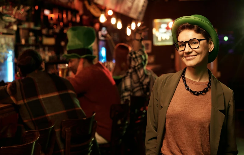 a woman wearing a green hat and glasses, happening, local bar, irish genes, inside a bar, lgbtq