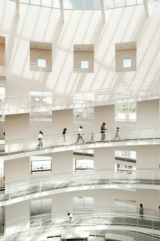 a group of people walking inside of a building, by Fei Danxu, trending on pexels, light and space, white building, balconies, issey miyake, spiral shelves full of books