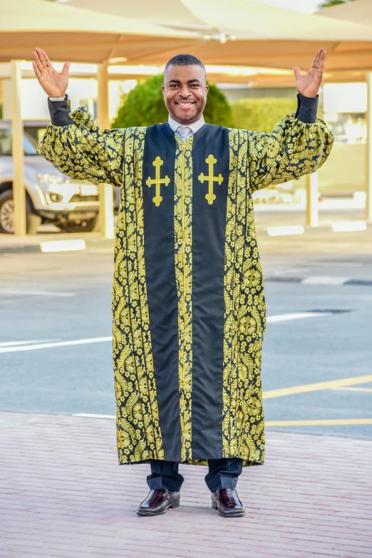 a man in a priest's robe standing in a parking lot, inspired by Edward Okuń, happening, black and yellow scheme, wearing ornate clothing, african ameera al taweel, very very happy