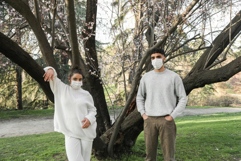 a man and a woman standing in front of a tree, by Nicolette Macnamara, pexels, renaissance, medical mask, wearing a white sweater, off - white collection, manuka