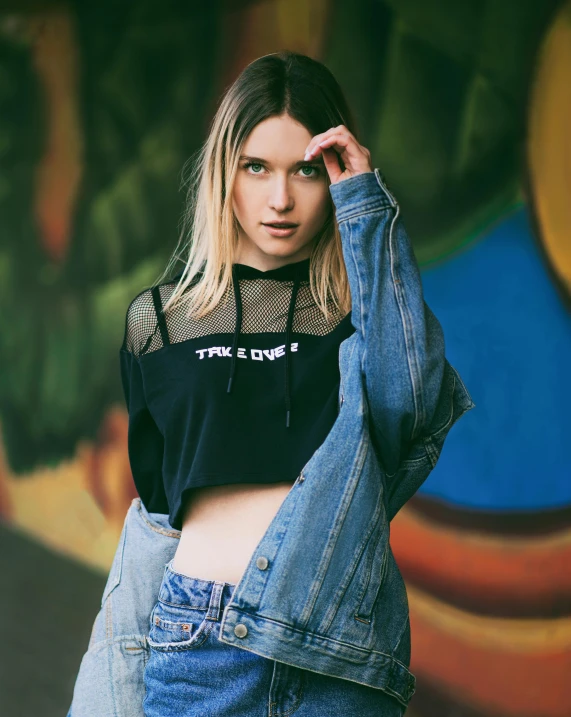 a woman standing in front of a graffiti wall, an album cover, inspired by Elsa Bleda, trending on unsplash, wearing jeans and a black hoodie, wearing a sexy cropped top, see - through, non binary model
