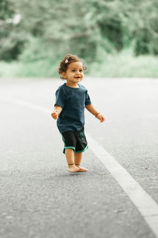 a small child standing in the middle of a road, wearing shorts and t shirt, teals, black, nivanh chanthara