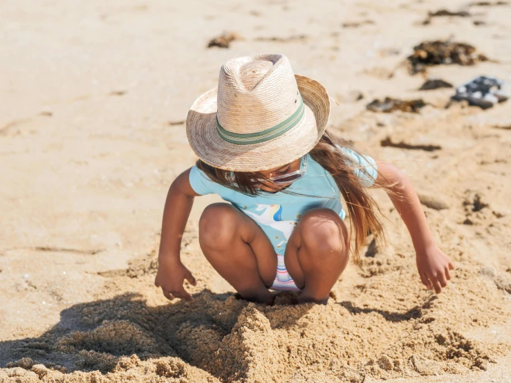 a little girl playing in the sand on the beach, by Arabella Rankin, pexels contest winner, beige fedora, thumbnail, high-quality photo, carefully designed