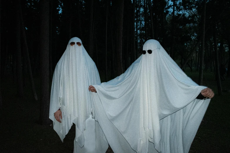 three people dressed in white standing in a forest, an album cover, by Attila Meszlenyi, pexels, halloween ghost under a sheet, adult pair of twins, wearing white suit and glasses, taken in the late 2010s