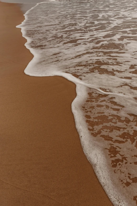 a large body of water sitting on top of a sandy beach, an album cover, unsplash, foamy waves, brown, up-close, serene