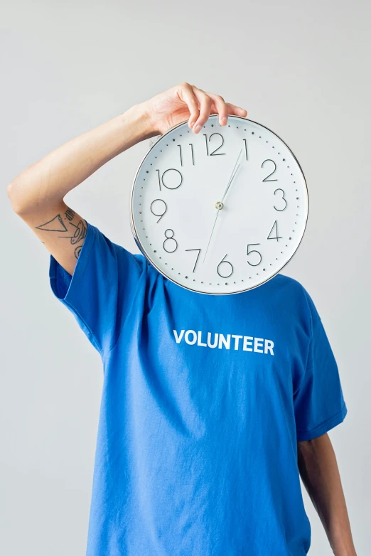 a man holding a clock in front of his face, by Julia Pishtar, trending on unsplash, tshirt, blue uniform, yearbook photo, humanity