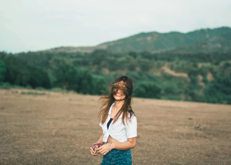 a woman standing in a field with her hair blowing in the wind, pexels contest winner, white shirt and green skirt, wide smile, vsco film grain, panoramic view of girl