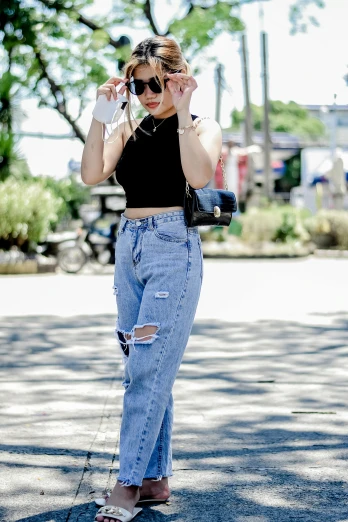 a woman standing on a street talking on a cell phone, a picture, by Robbie Trevino, trending on pexels, wearing a cropped top, baggy jeans, in style of lam manh, kylie jenner
