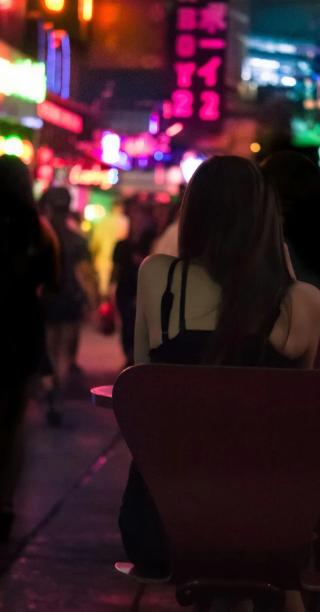 a woman sitting on a bench in a city at night, trending on unsplash, in a nightclub, bangkok, transgender, colorful crowd