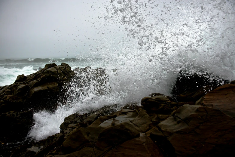 a man riding a surfboard on top of a wave, inspired by Winslow Homer, pexels contest winner, with jagged rocks & eerie, downpour, cornwall, water particles