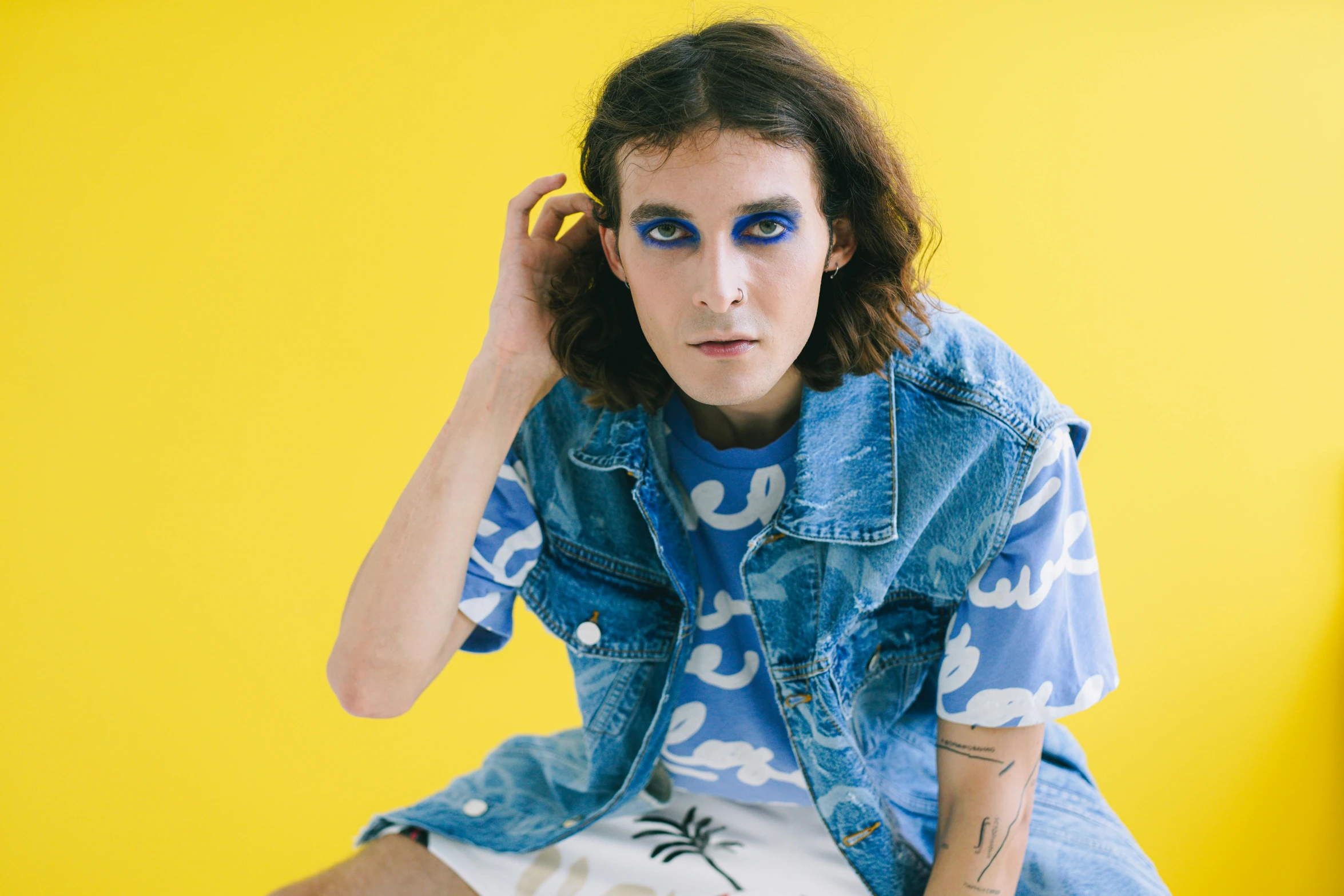 a woman sitting on top of a bed next to a yellow wall, an album cover, by Ellen Gallagher, trending on pexels, graffiti, androgynous face, blue body paint, patterned clothing, a photo of a man