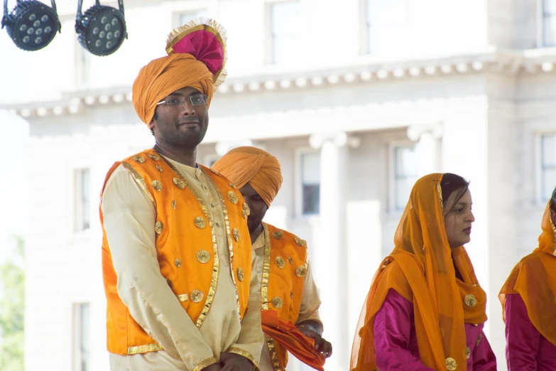 a group of men in turbans standing next to each other, by Manjit Bawa, hurufiyya, orange and yellow costume, square, person in foreground, couple