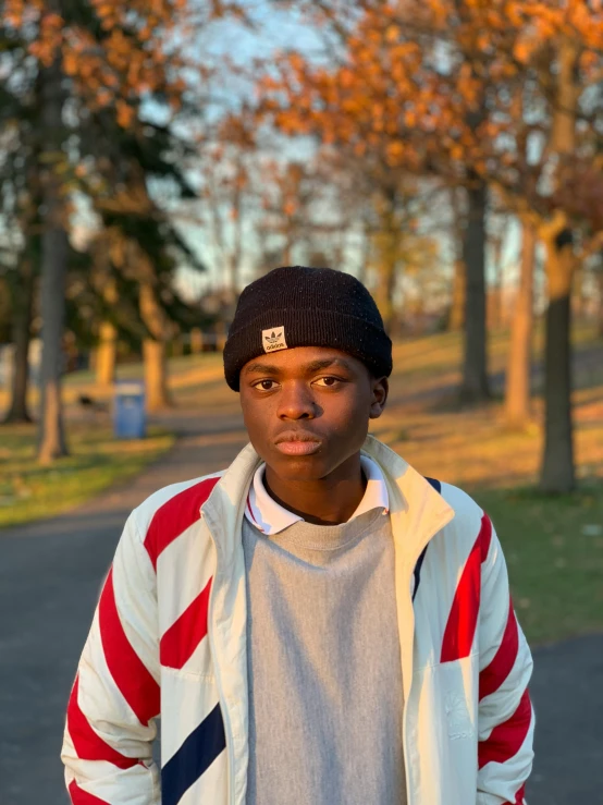 a young man standing in a park with a skateboard, by Andrew Stevovich, dark skinned, 2022 photograph, dark blue beanie, portait image