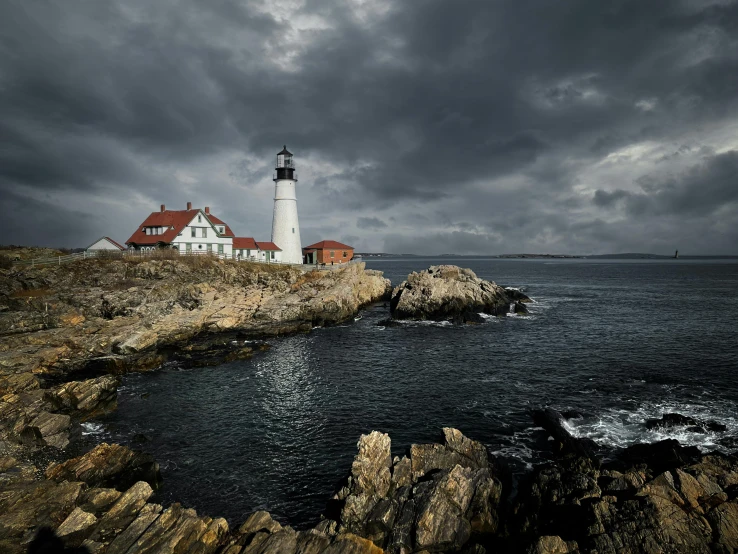 a lighthouse on a rocky shore under a cloudy sky, by Andrew Domachowski, pexels contest winner, new england architecture, on a dark background, dramatic”