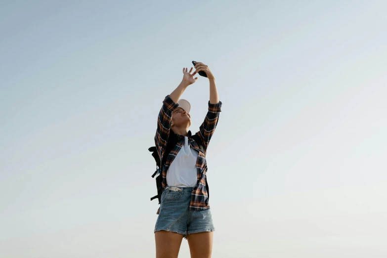 a woman standing on top of a sandy beach, trending on pexels, happening, phone!! held up to visor, wearing a plaid shirt, shot in the sky, wearing shorts and t shirt